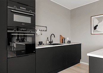 Modern kitchen with black cabinetry, white countertops, built-in oven, sink with a black faucet, and minimal decor. A framed abstract artwork hangs on a gray wall.