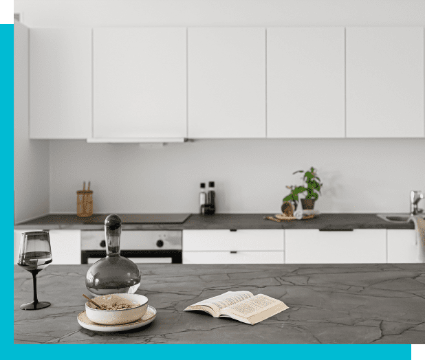 Modern kitchen with white cabinets, a dark gray countertop, and a gray island featuring a decanter, wine glass, bowl with oats, and an open book. A few kitchen items are arranged by the backsplash.