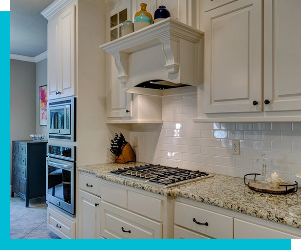 A modern kitchen with white cabinets, a granite countertop, stainless steel oven, and gas stovetop, with various decorative items on the shelves and counter.