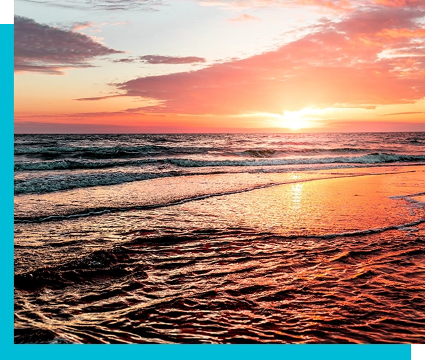 A vibrant sunset with a mix of pink, orange, and purple hues reflects on the waves and wet sand of a beach.